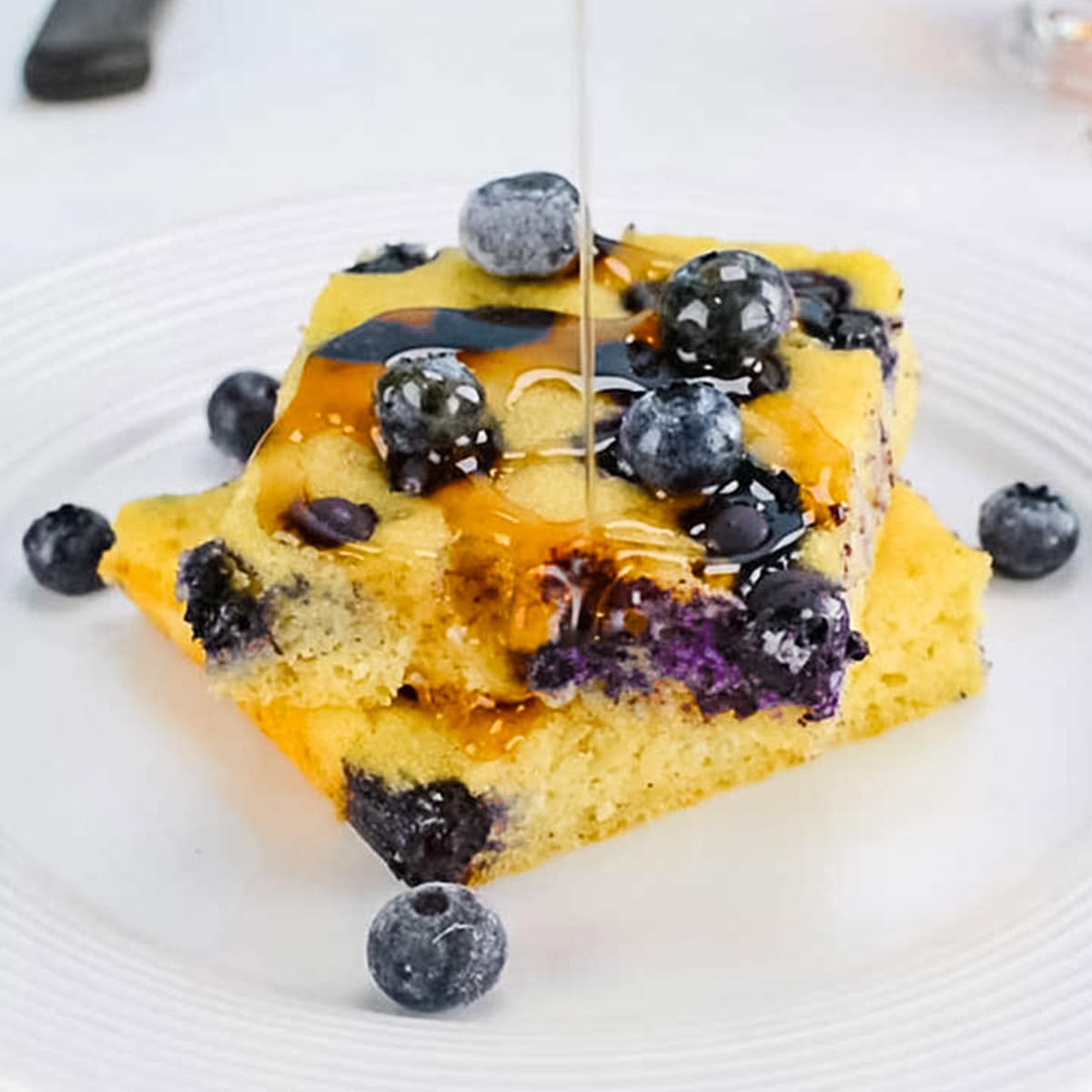 Keto sheet pan pancakes with blueberries and maple syrup on a white plate.