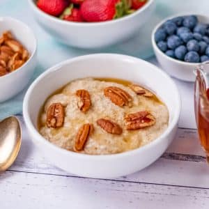 Keto porridge in a white bowl topped with pecan nuts.