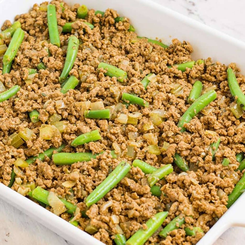 Keto cottage pie first layer of ingredients in a white baking dish.