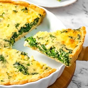 A slice of keto spinach quiche on w white pie dish.