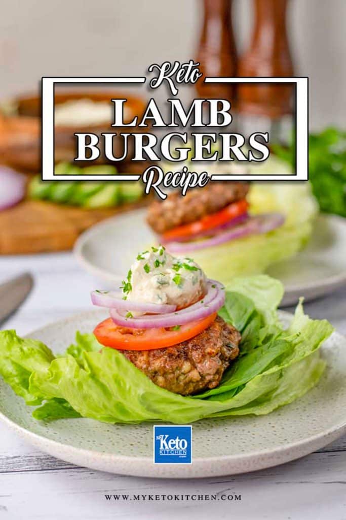 Keto lamb burger patty on a white plate with a lettuce leaf topped with tomato, onion and sauce.