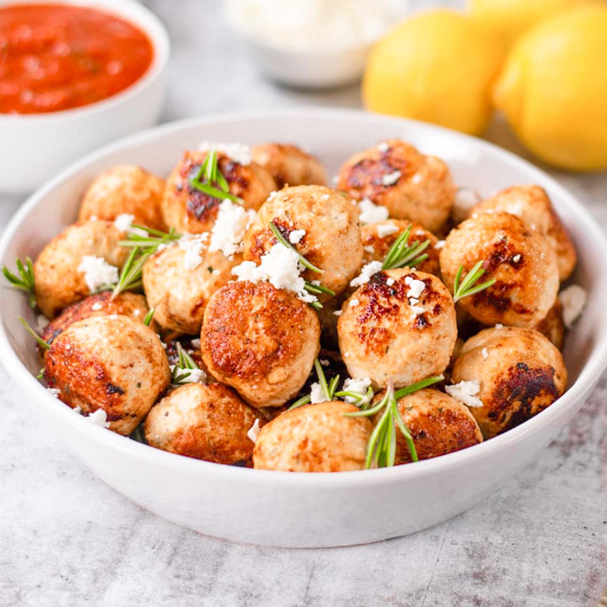 Keto chicken and feta meatballs in a white bowl with lemon and marina sauce.