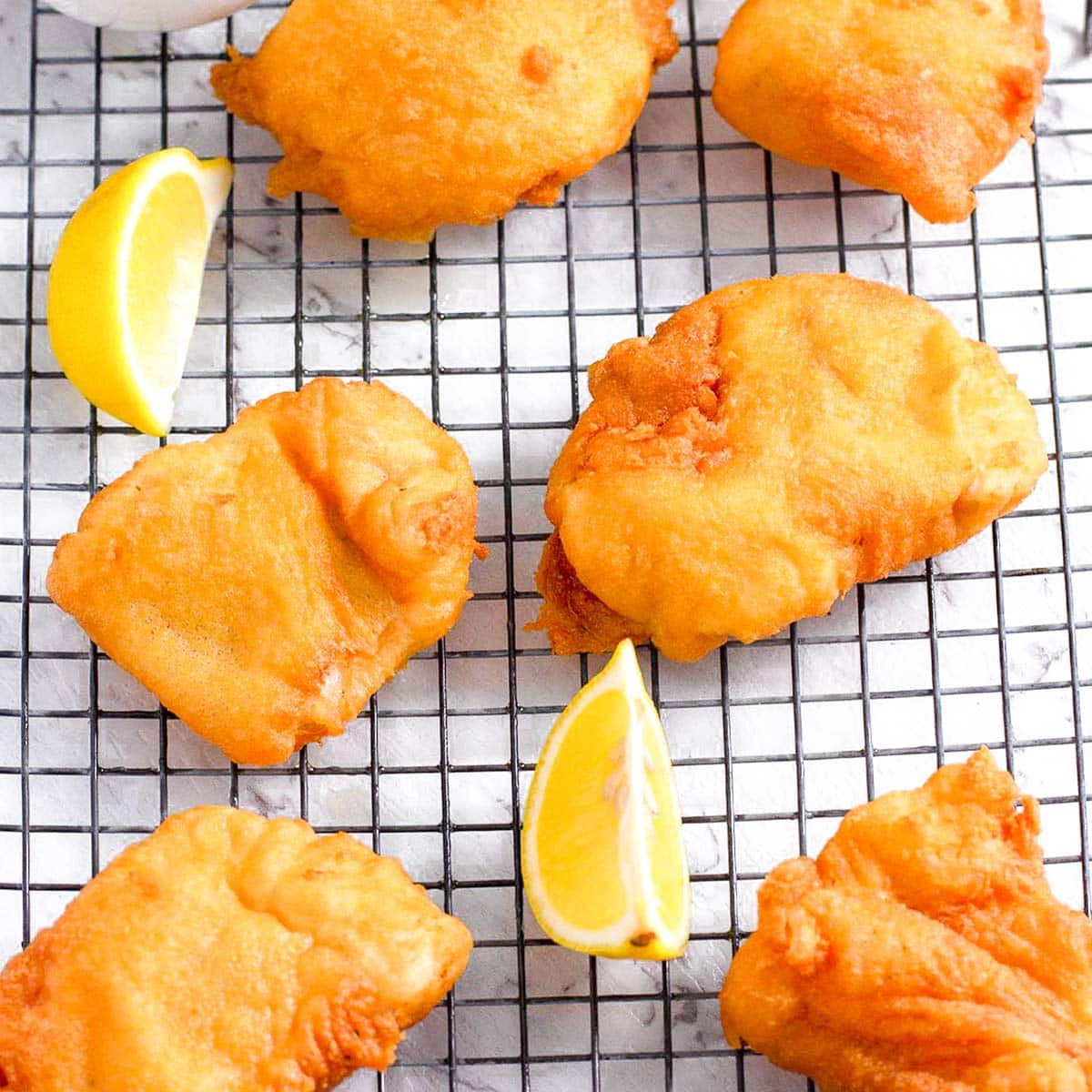 keto battered fish on a cooling rack with lemon wedges.